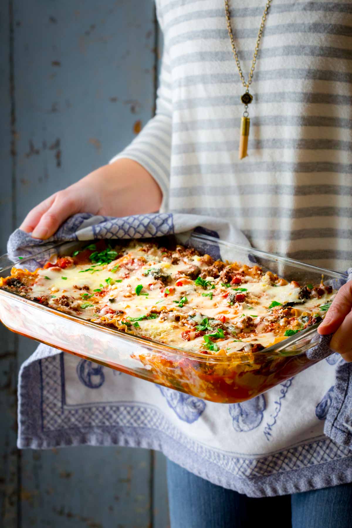 someone's torso holding the lasagna with a blue and white dish cloth