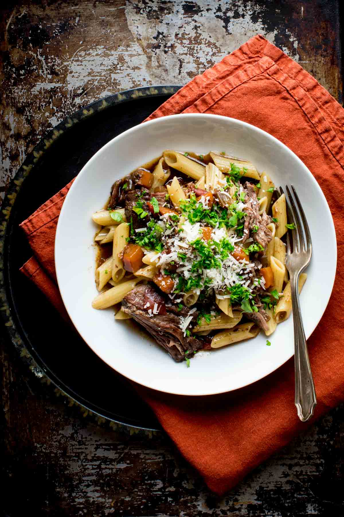 the pasta with beef in a white bowl on a charger with an orange napkin