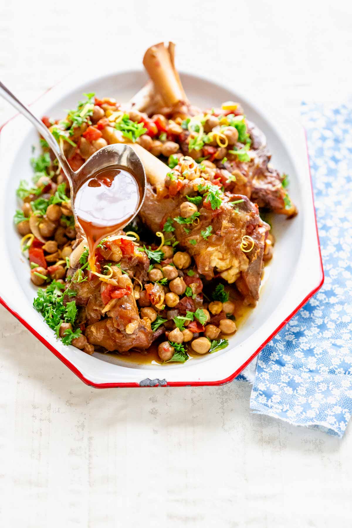 a platter of lamb shanks with the gravy being ladled over it