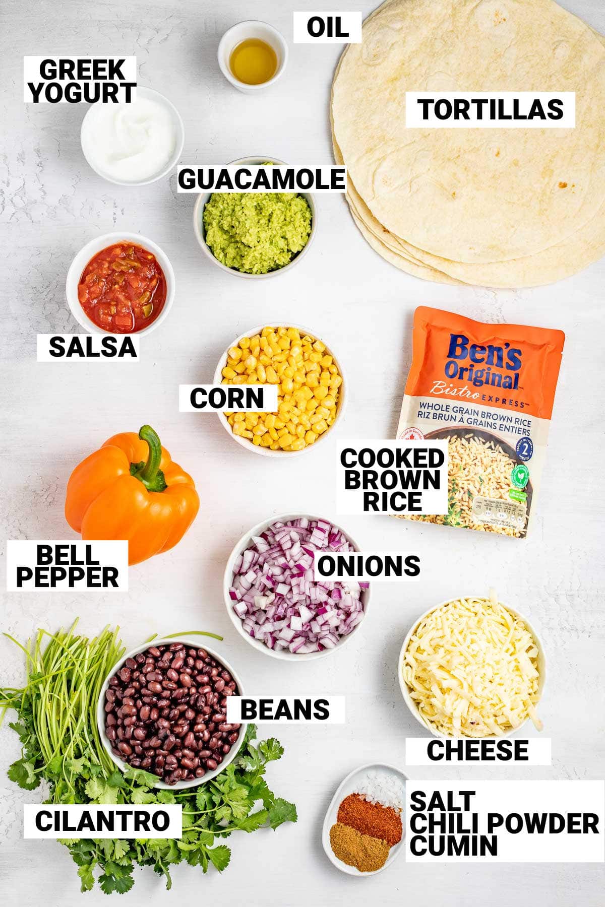 tortillas, guacamole, salsa, corn, brown rice, bell peppers, onions, beans, cheese, cilantro, and seasonings laid out on a table