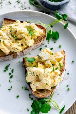 healthy egg salad on two pieces of bread with dill and chives as garnish and seasoning