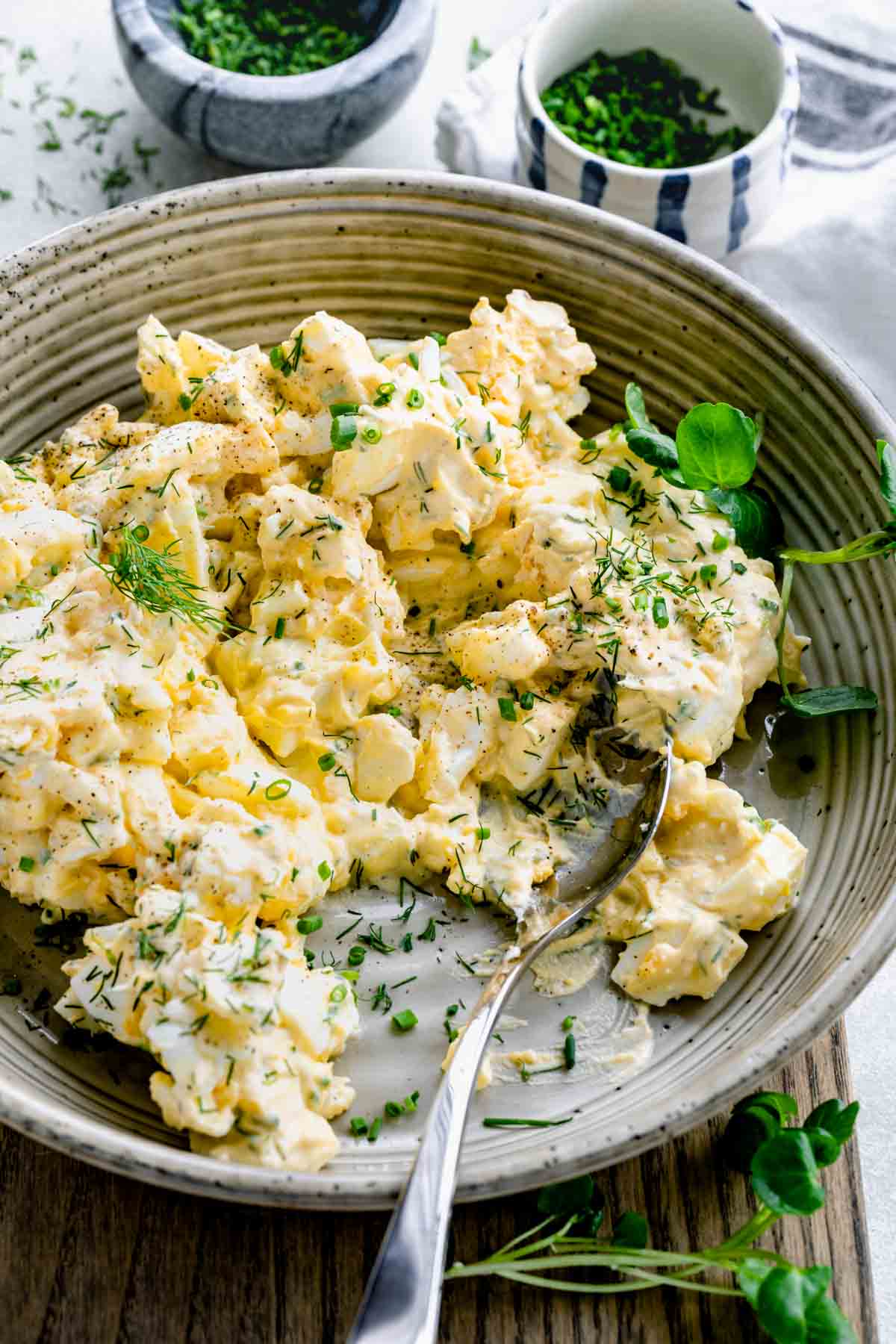 a ceramic bowl with the egg salad mixed in it with a spoon