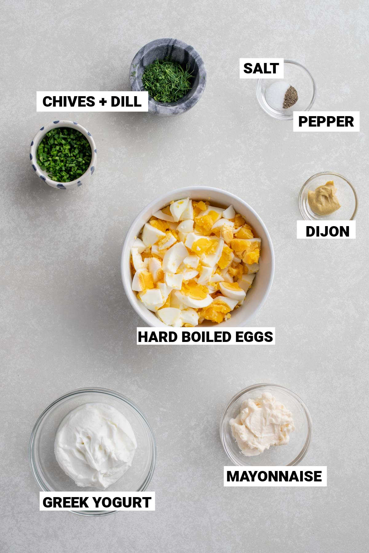 chivies, dill, salt, pepper, chopped hard boiled eggs, dijon, greek yogurt, and mayonnaise mise en place