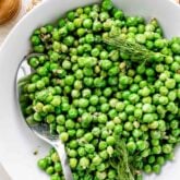 a white bowl with cooked peas, a spoon and sprigs of dill