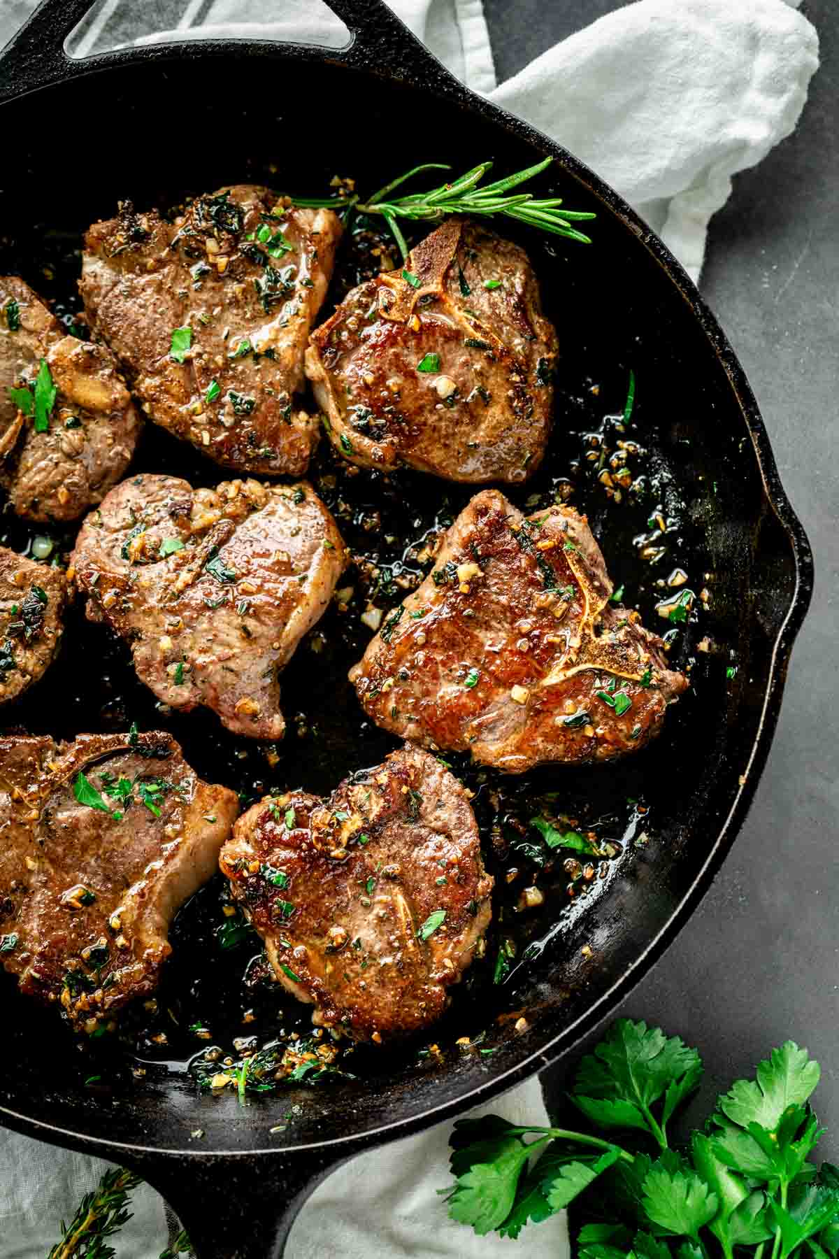 a cast iron skillet with lamb chops with fresh herbs on a white napkin on a gray table