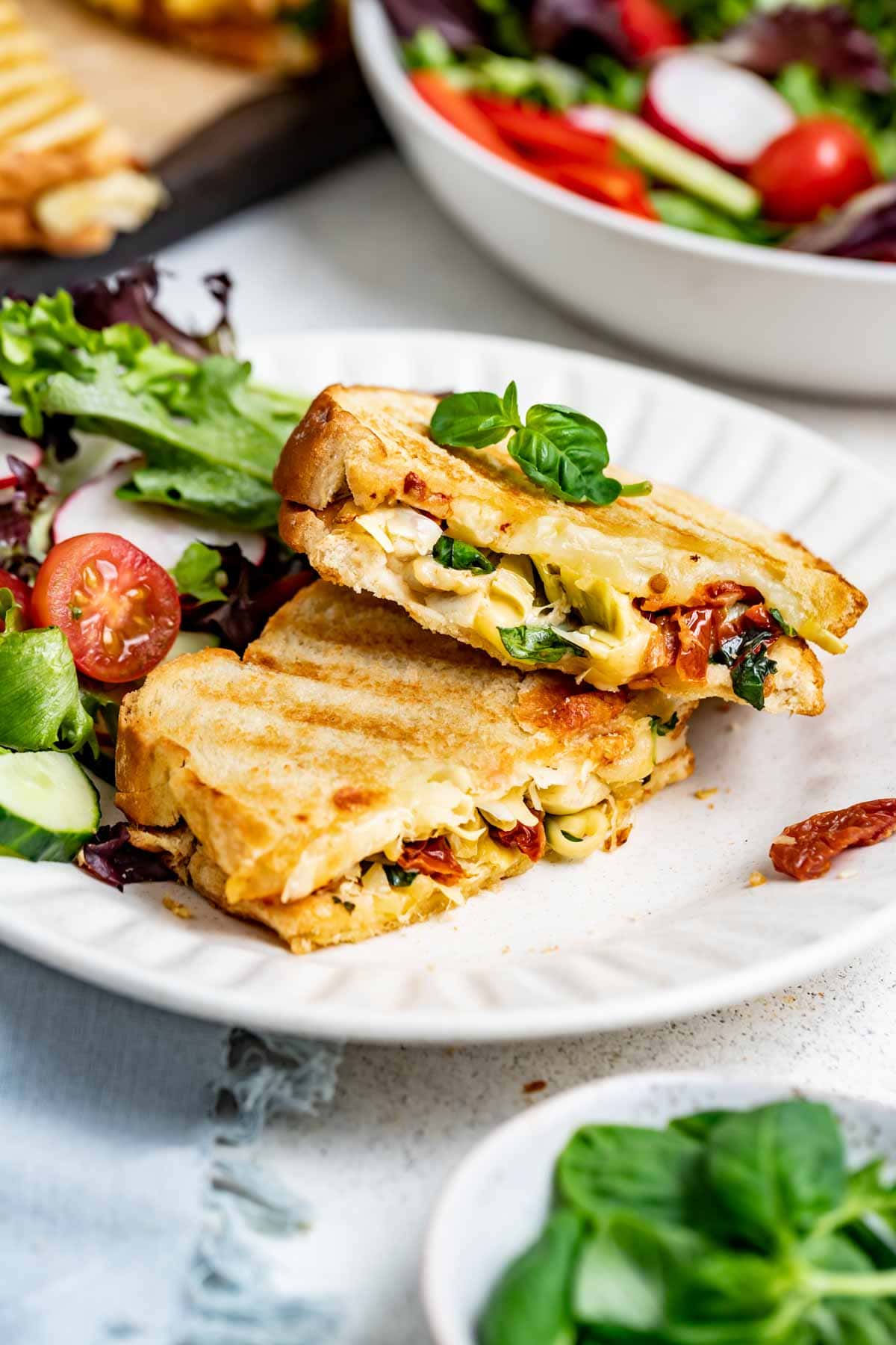 veggie panini with sun dried tomatoes and cheese cut in half with a side salad beside it