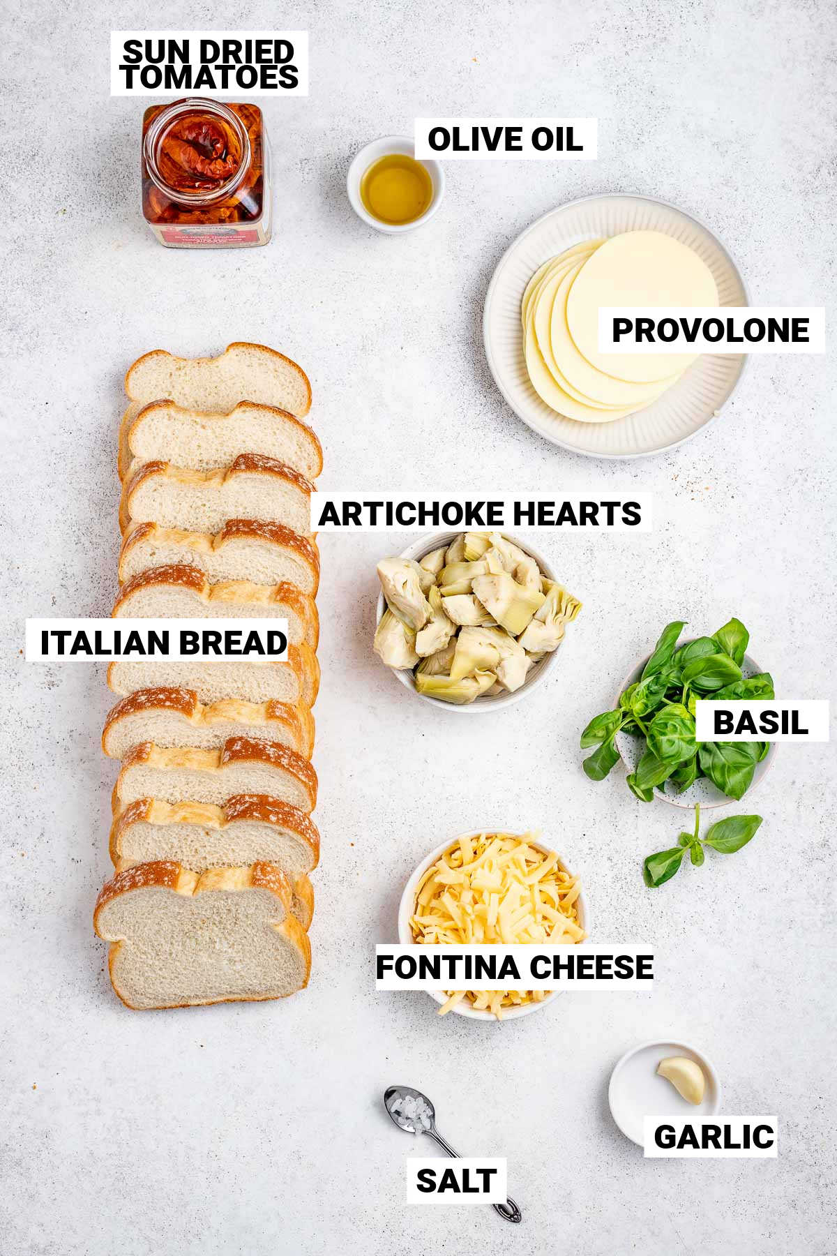 italian bread, fontina cheese, garlic, salt, basil, artichoke hearts, and sun dried tomatoes laid out to make vegetarian paninis