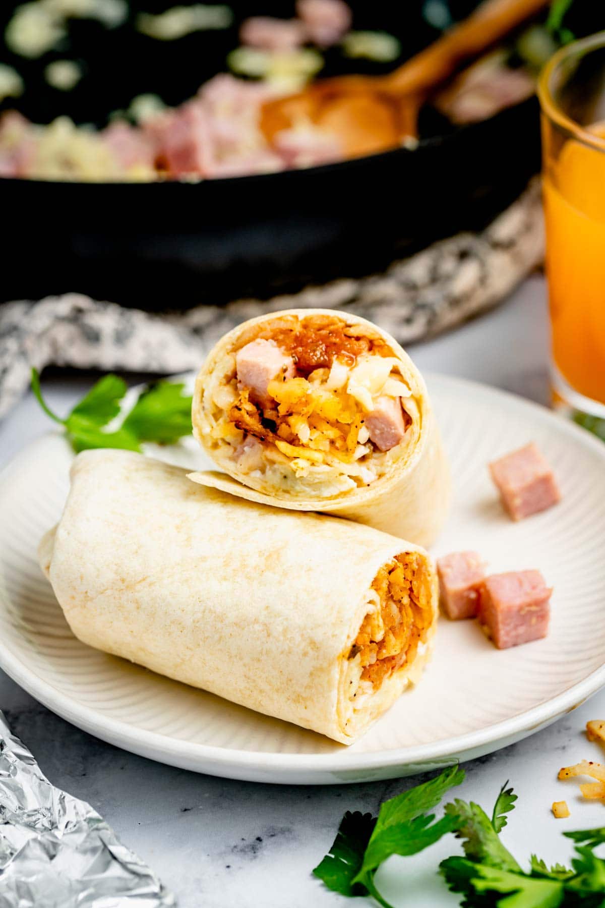 breakfast burrito with ham cut in half on circular white plate