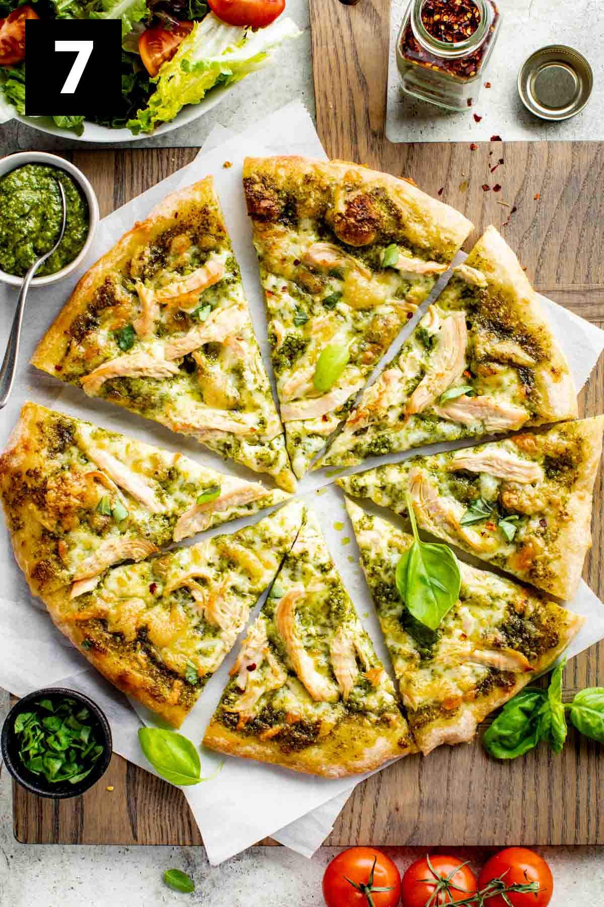 overhead of the pizza cut into 8 wedges on parchment with a bowl of pesto