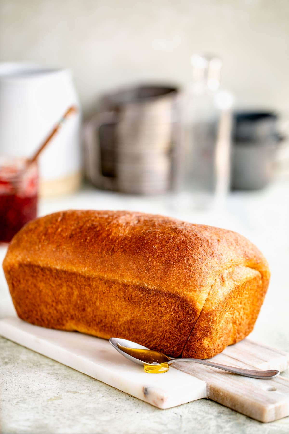 a golden brown loaf of honey wheat homemade bread with a spoonful of honey sitting in front of it