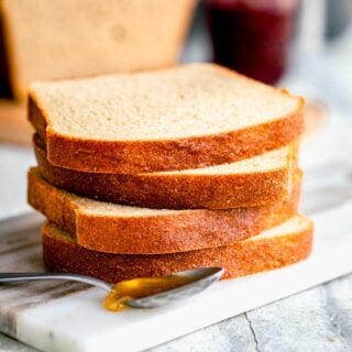 honey wheat bread sliced and piled on top of multiple slices with a spoonful of honey in the foreground