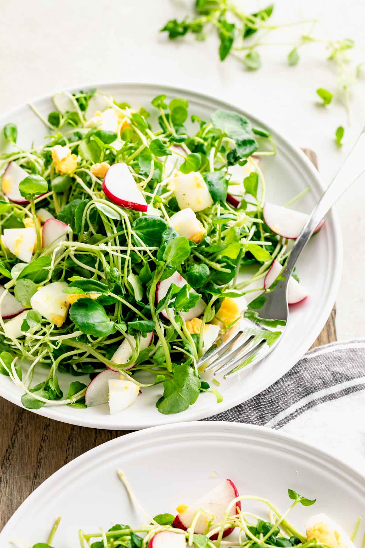 dressed watercress salad in circular white plate with fork