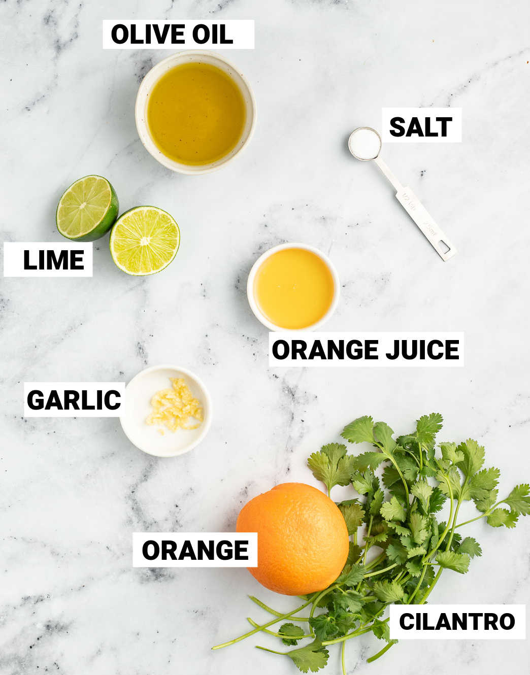 oil, salt, lime, orange juice, garlic, orange, and cilantro laid out on a marble surface to make the dressing for salmon salad