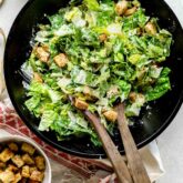 a black wooden salad bowl with creamy Cesar salad in it.