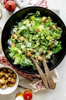 a black wooden salad bowl with creamy Cesar salad in it.