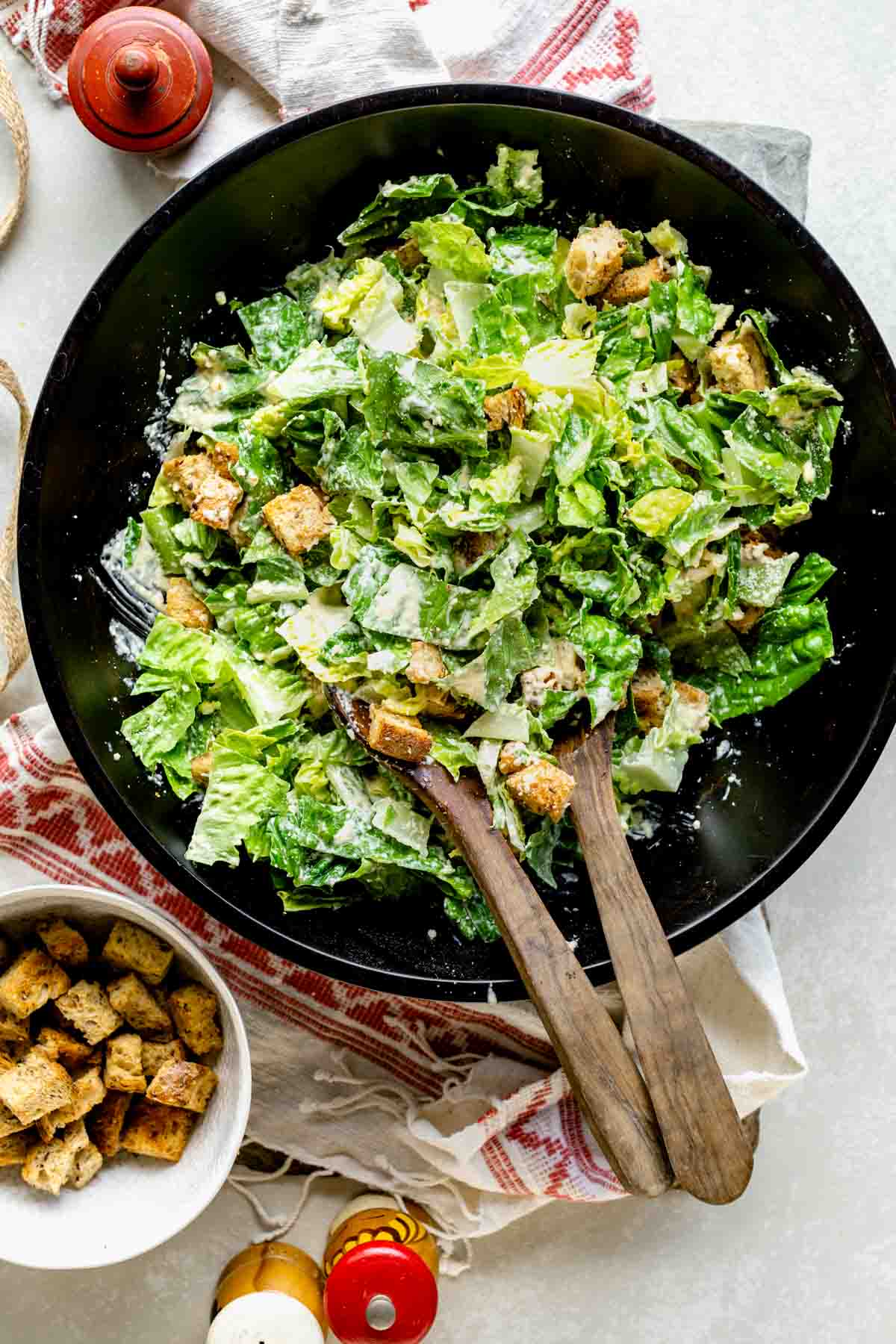 a black wooden salad bowl with creamy Cesar salad in it.