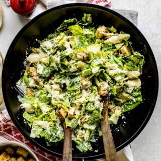 the caesar salad in a black bowl with wooden salad tongs