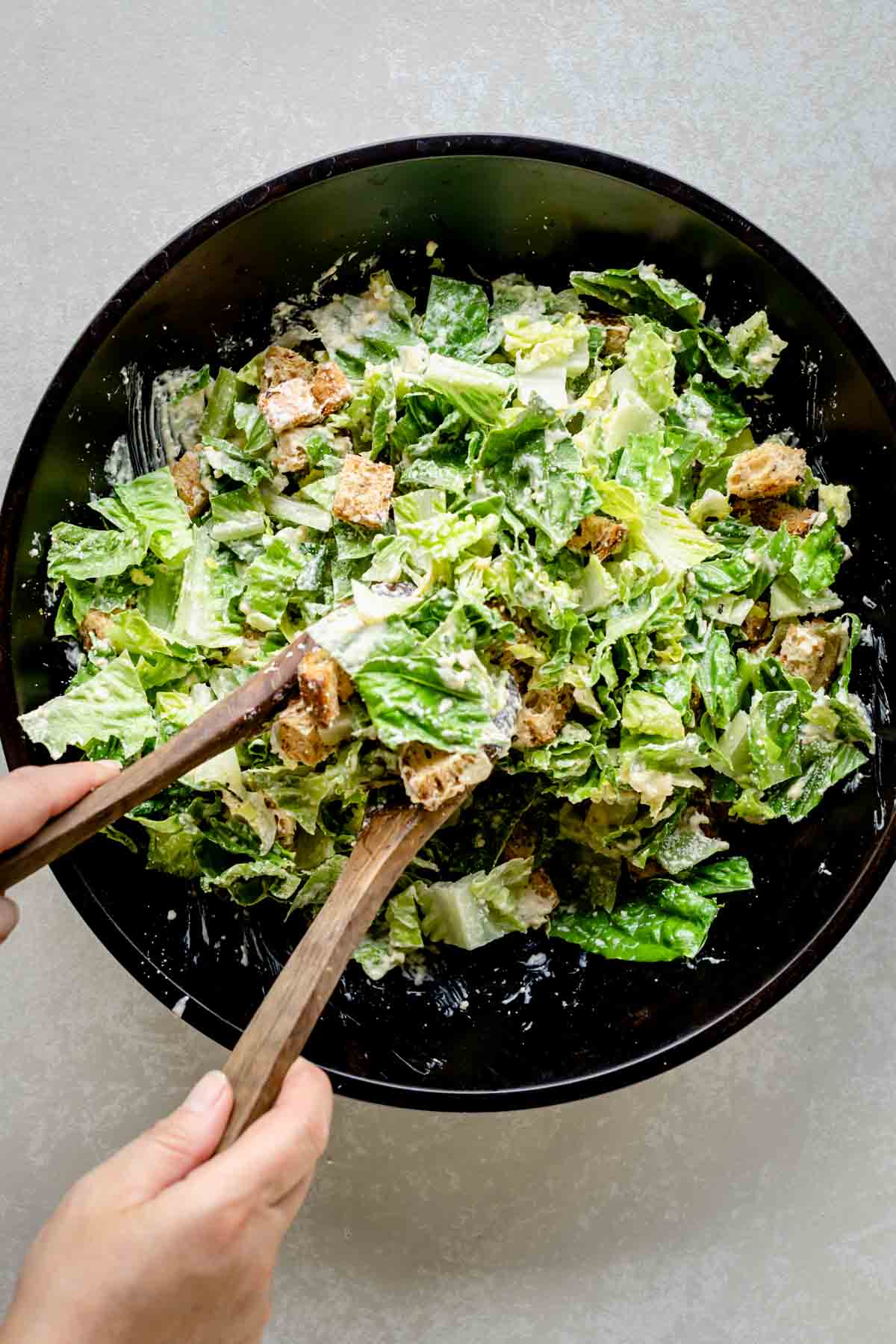 the cesar being tossed with wooden salad tongs