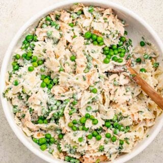 salmon pasta salad with pee in a large white bowl and a wooden spoon set on the side