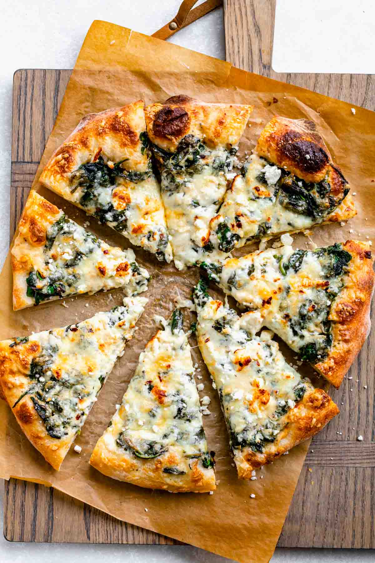 overhead view of spinach pizza cut into triangles on a pizza board