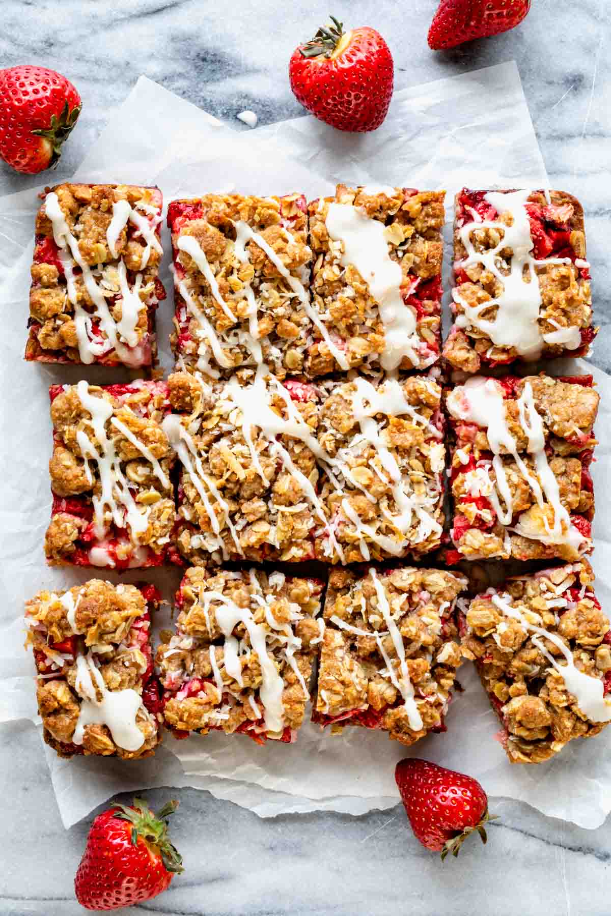the strawberry oatmeal bars on a piece of parchment paper all cut into squares and drizzled with lemon icing