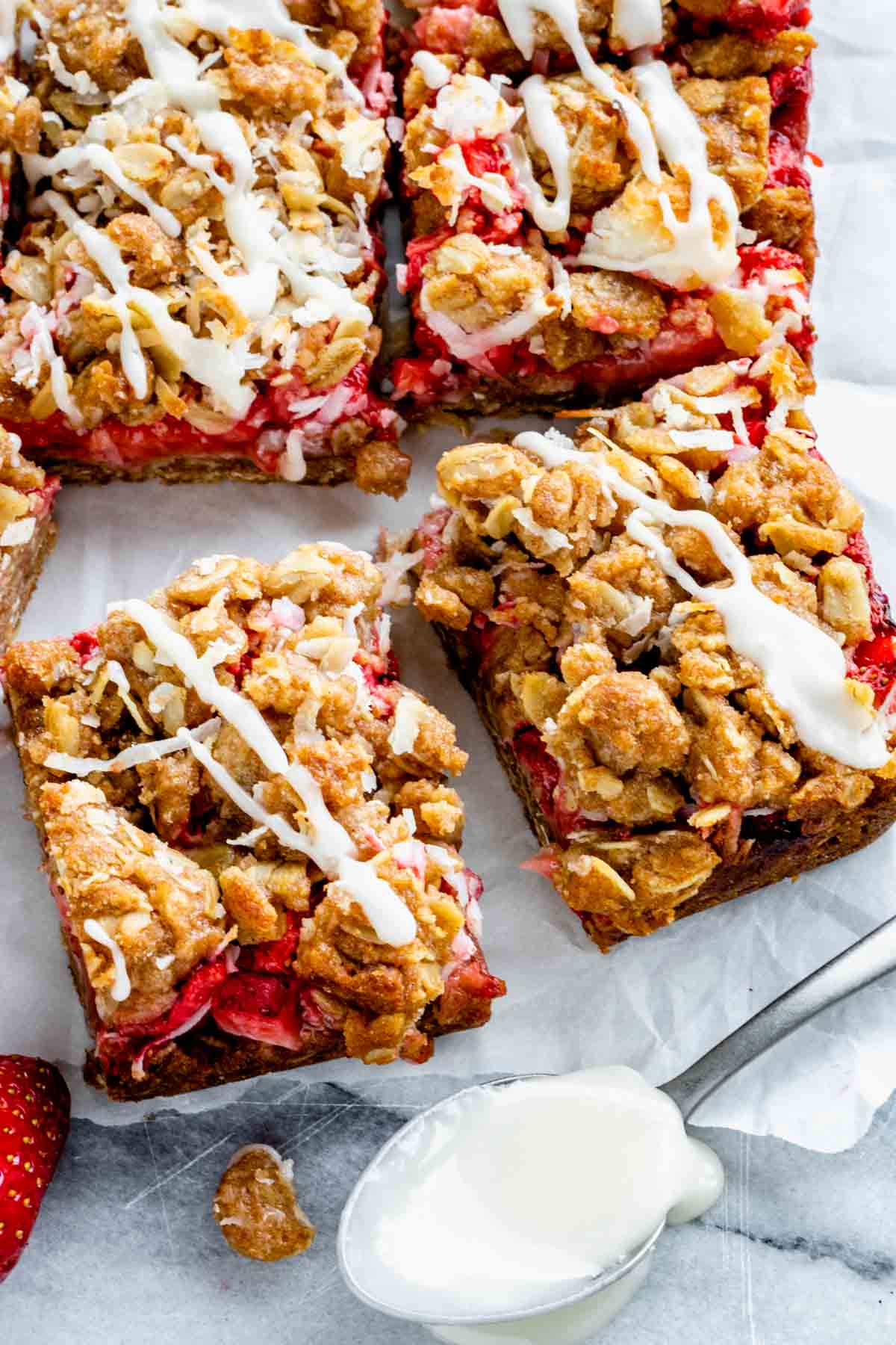 up close shot of two strawberry oatmeal crumble bars with lemon glaze on top and a spoonful of glaze in the foreground