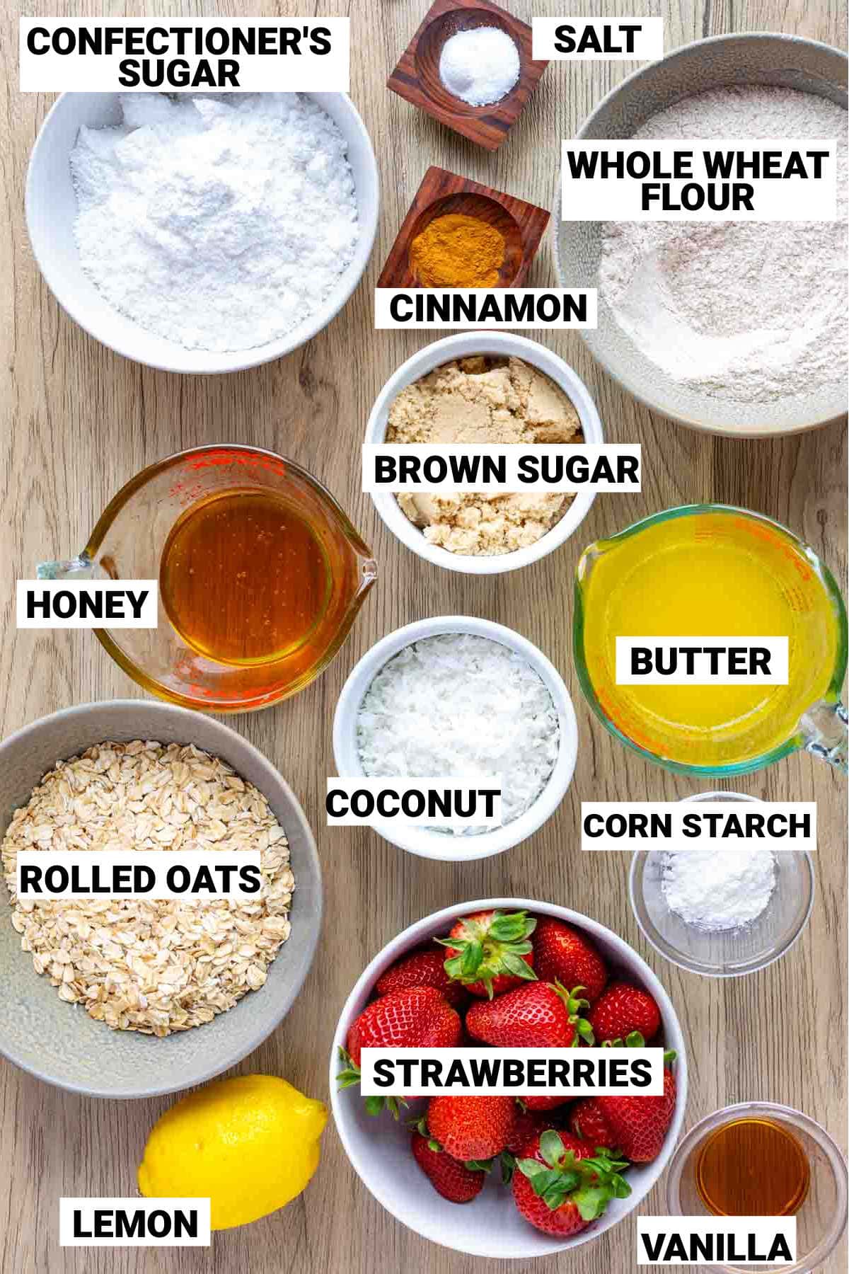 confectioner's sugar, salt, whole wheat flour, cinnamon, brown sugar, honey, coconut, melted butter, corn starch, rolled oats, strawberries, lemon, and vanilla all measured out individually to make strawberry oat bars