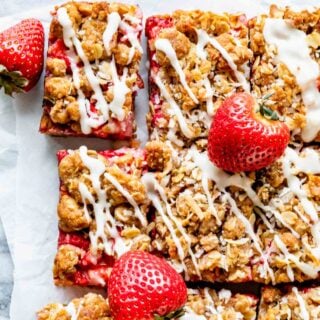 strawberry oat bars with lemon glaze and whole strawberries scattered around