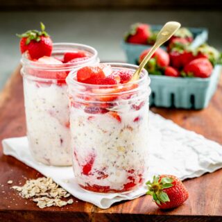 two mason jars full of strawberry overnight oats on a wooden surface