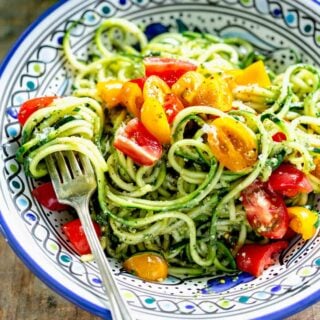 spiralized zucchini noodles tossed with peso and topped with cherry tomatoes in a bowl with a fork
