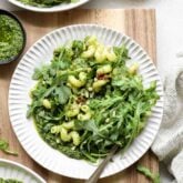 overhead photo of arugula pasta on a circular white plate on a wooden cutting board