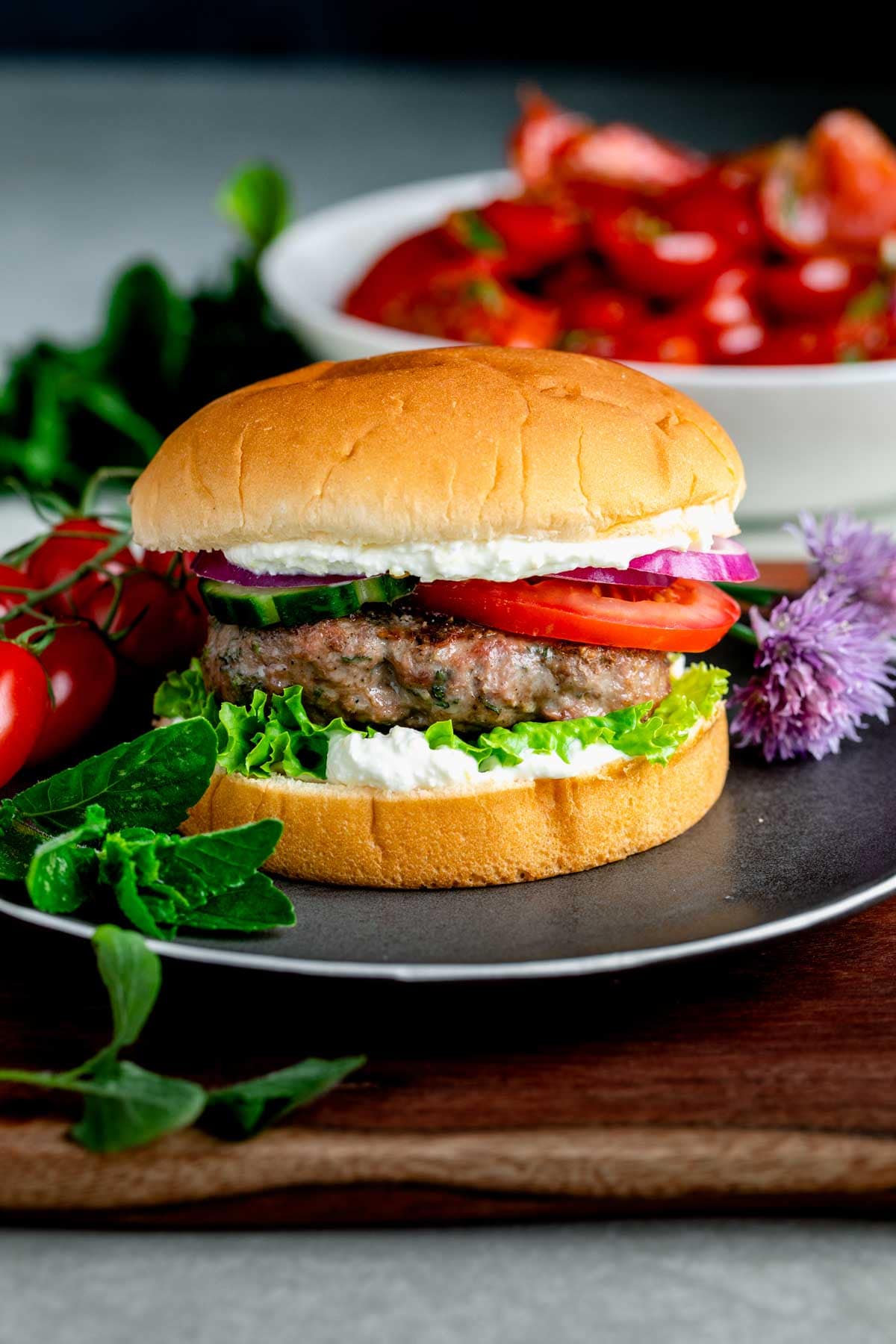 a lamb burger on a black plate with tomato salad in the background