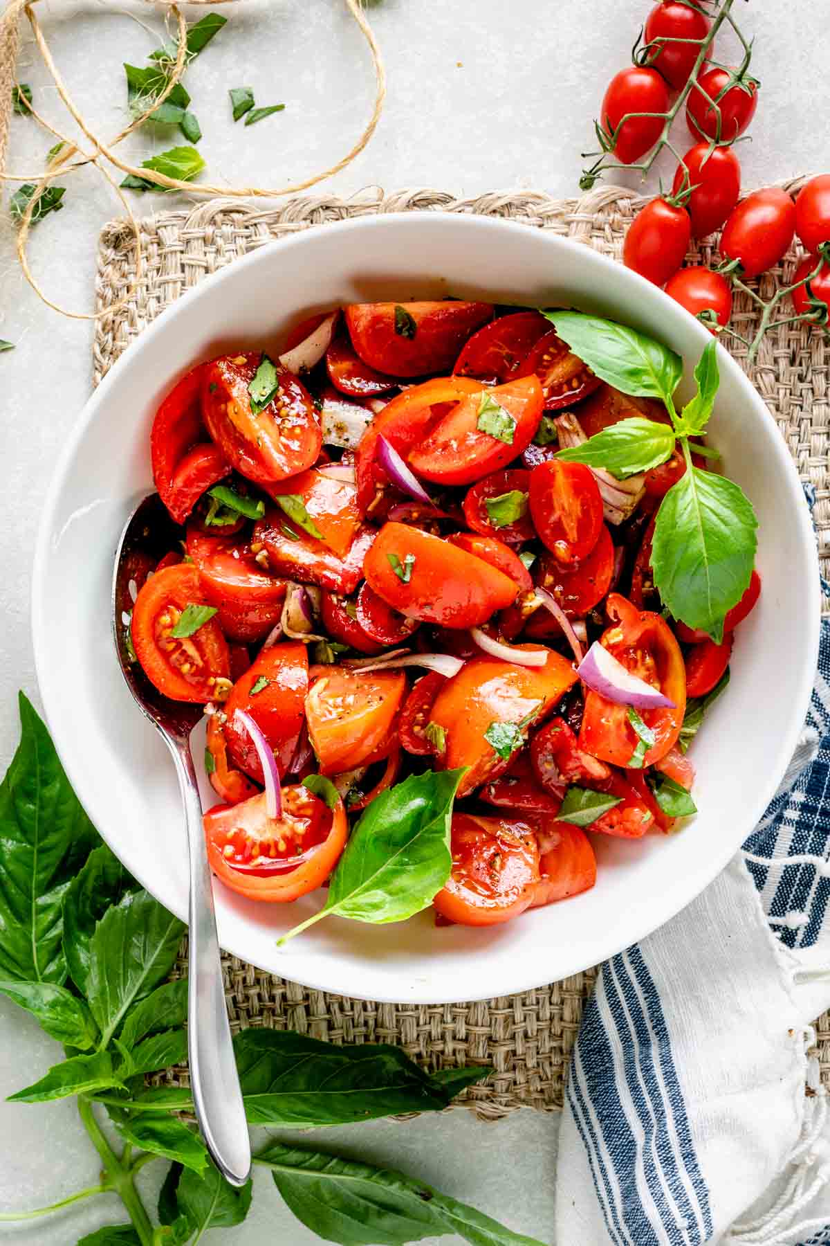 tomato salad with balsamic vinaigrette in a white bowl from overhead with cherry tomatoes on the table and basil sprigs
