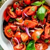 close up of the tomato wedge salad with basil sprig in a white bowl with serving spoon