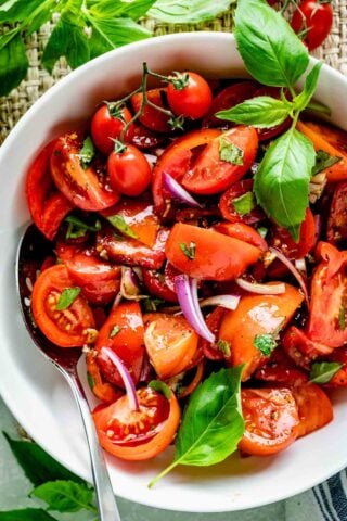 close up of the tomato wedge salad with basil sprig in a white bowl with serving spoon