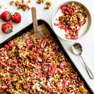 homemade strawberry granola in a sheet pan and with a white bowl of it with milk off to the side