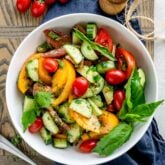 tomato cucumber salad in a white bowl from overhead with a cluster of grape tomatoes and a pepper grinder