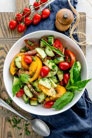 tomato cucumber salad in a white bowl from overhead with a cluster of grape tomatoes and a pepper grinder