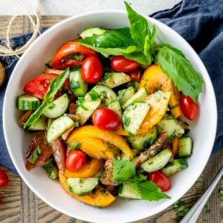 tomato and cucumbers in a white bowl with basil