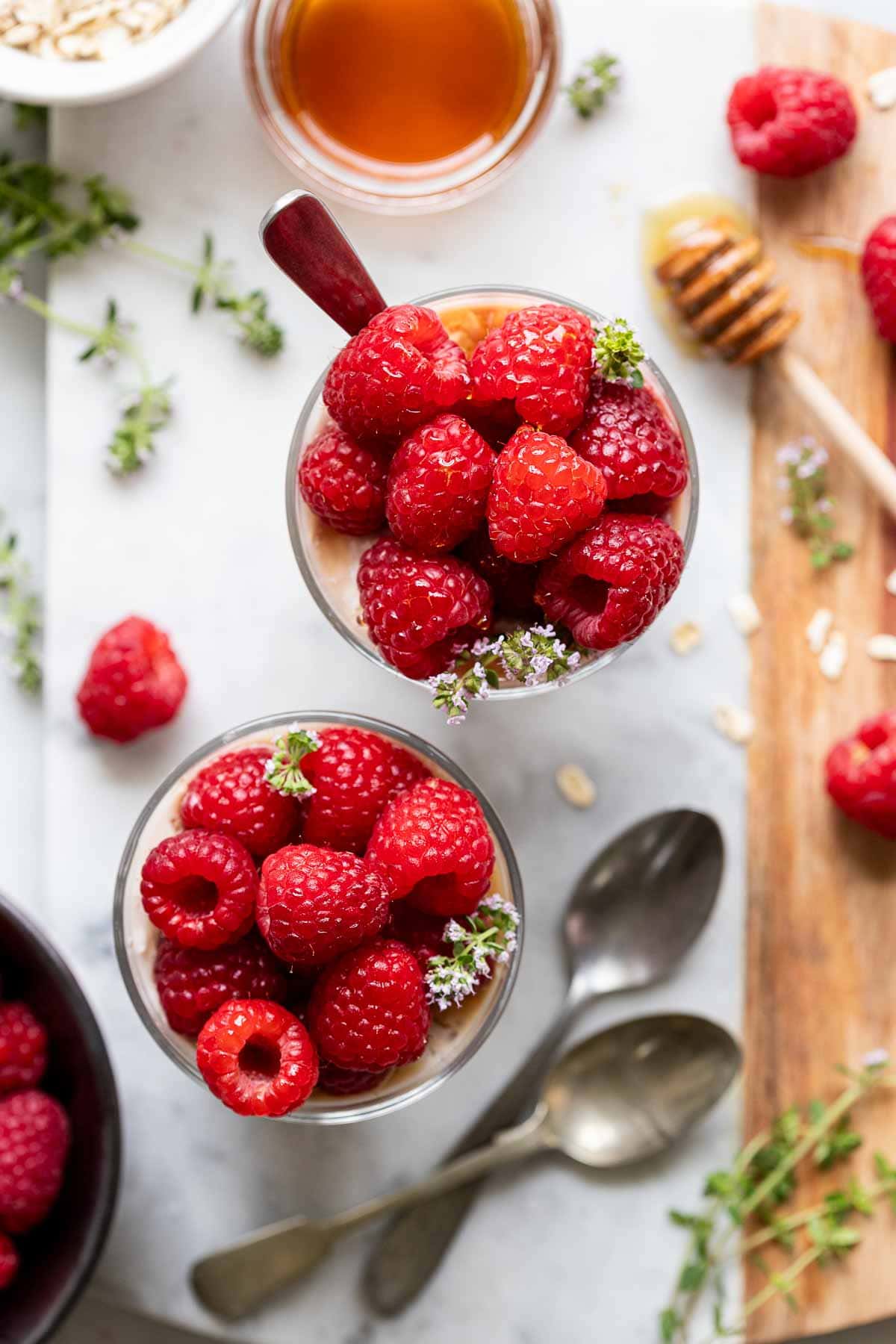 overhead shot of two overnight oats with raspberries on a white counter and topped with fresh raspberries.