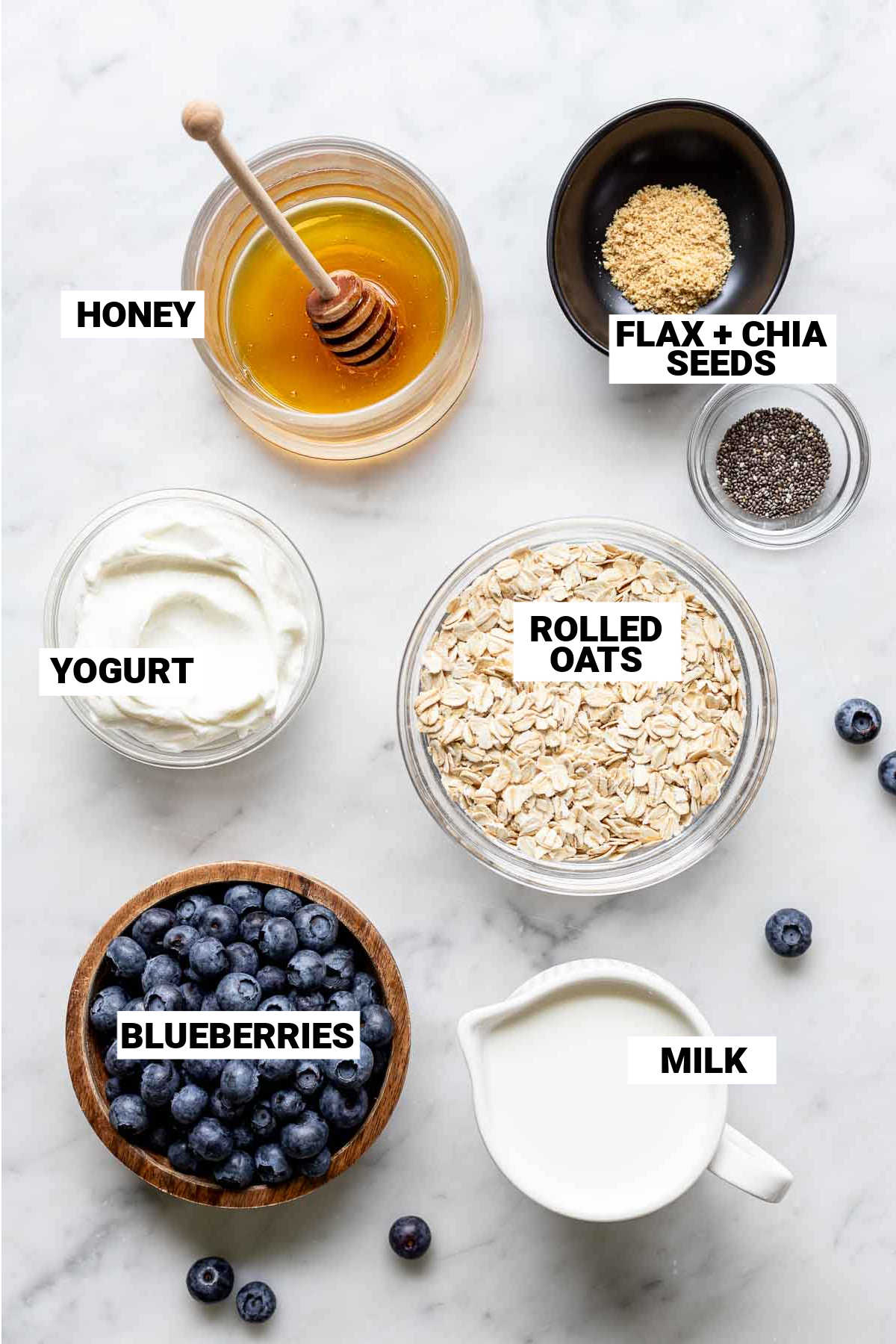 ingredients for blueberry overnight oats: honey, flax and chia seeds, rolled oats, greek yogurt, blueberries, and milk