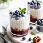 blueberry overnight oats in a layer with mashed blueberries on the bottom, oats in the middle, and fresh blueberries with garnish on the top