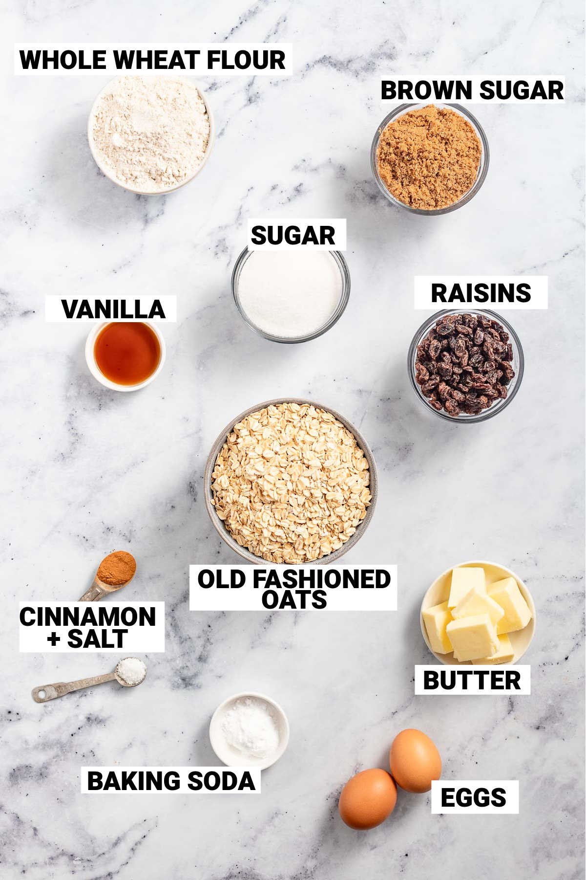 the ingredients to make healthy whole wheat oatmeal cookies including whole wheat flour, brown sugar, sugar, vanilla, raisins, old-fashioned oats, cinnamon, salt, butter, baking soda, and eggs.