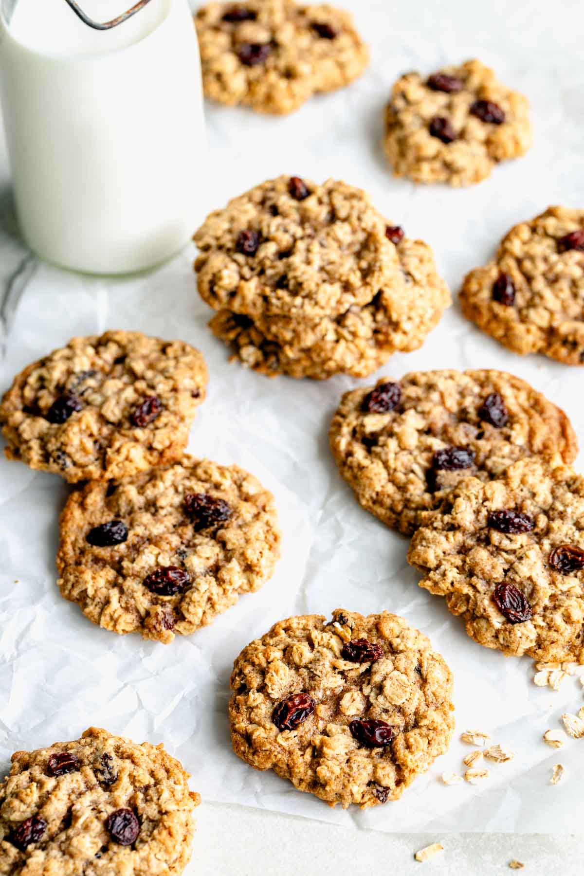 oatmeal raisin cookies scattered on a sheet of parchment paper with a jug of milk next to them