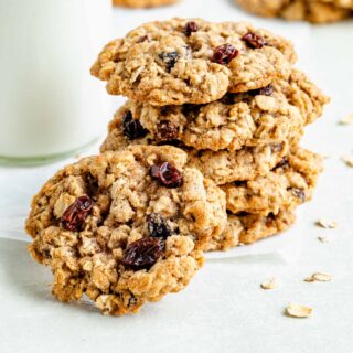 a few whole wheat oatmeal raisin cookies stacked on top of each other on a piece of parchment with a glass of milk on the left in the background