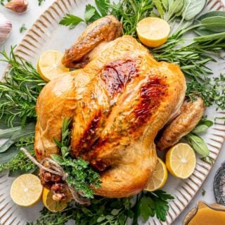 the chicken overhead on a platter with rosemary and sage sprigs and lemon halves