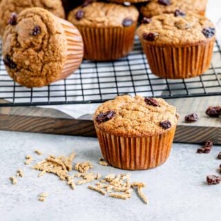 bran muffin on the kitchen counter with all bran cereal on the counter in front of it and more muffins behind it