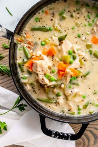 creamy turkey soup in a black stew pot with a ladle lifting out a serving