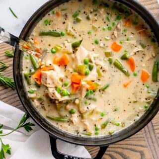 creamy turkey soup in a black stew pot with a ladle lifting out a serving