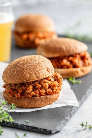 three ground turkey sloppy joes with a glass of orange drink out of focus on the left